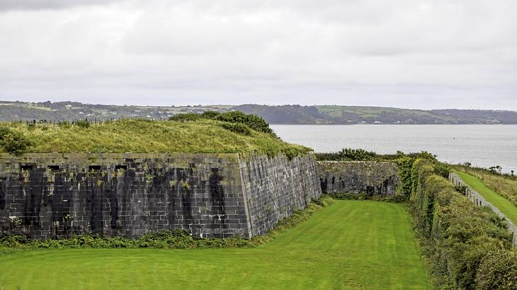 Brick structure covered in and surrounded by greenery, overlooking a sea