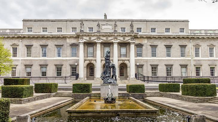 A statue and water fountain in front of a structure with four columns