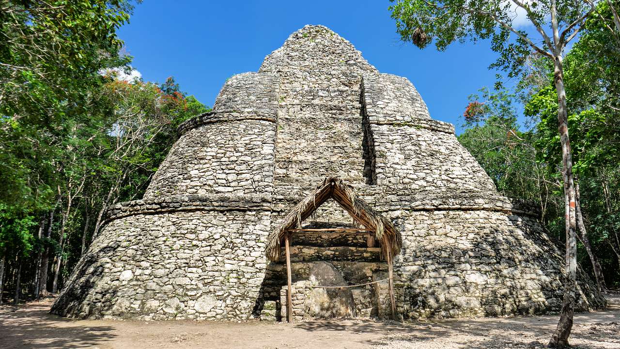 A pyramid made out of stone surrounded by trees under a blue sky