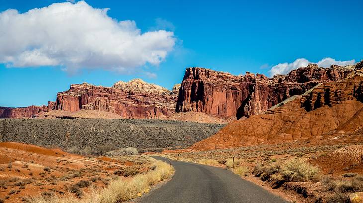 A paved road leading to red rocky cliffs at the back with blue sky above A paved road leading to red rocky cliffs at the back with blue sky above