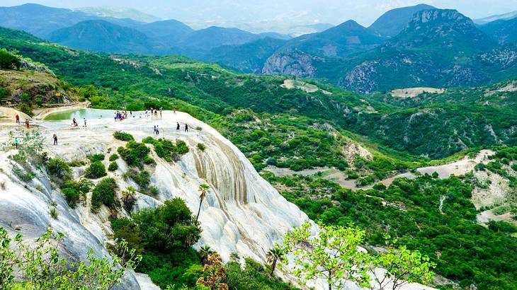 A waterfall-like rock formation with a hot spring, surrounded by rolling green hills