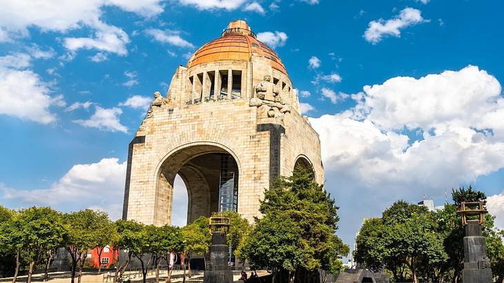 A monument with a tall arch on each side and an orange dome under a partly cloudy sky