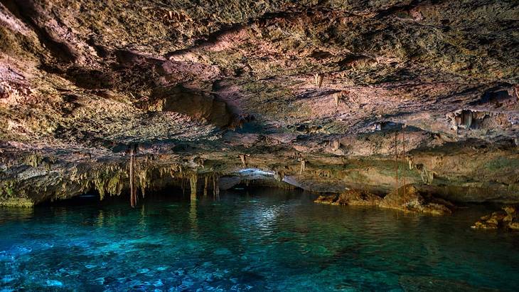 The inside of a lit up cave with visible clear blue water below