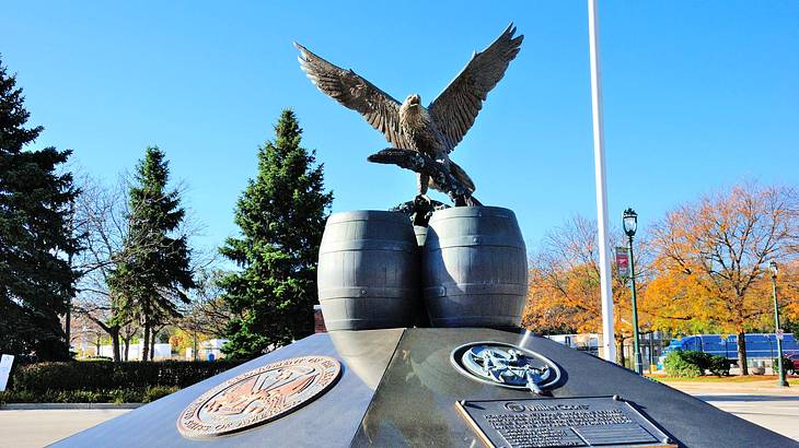 A statue of an eagle sitting on kegs on top of a marble pedestal with seals