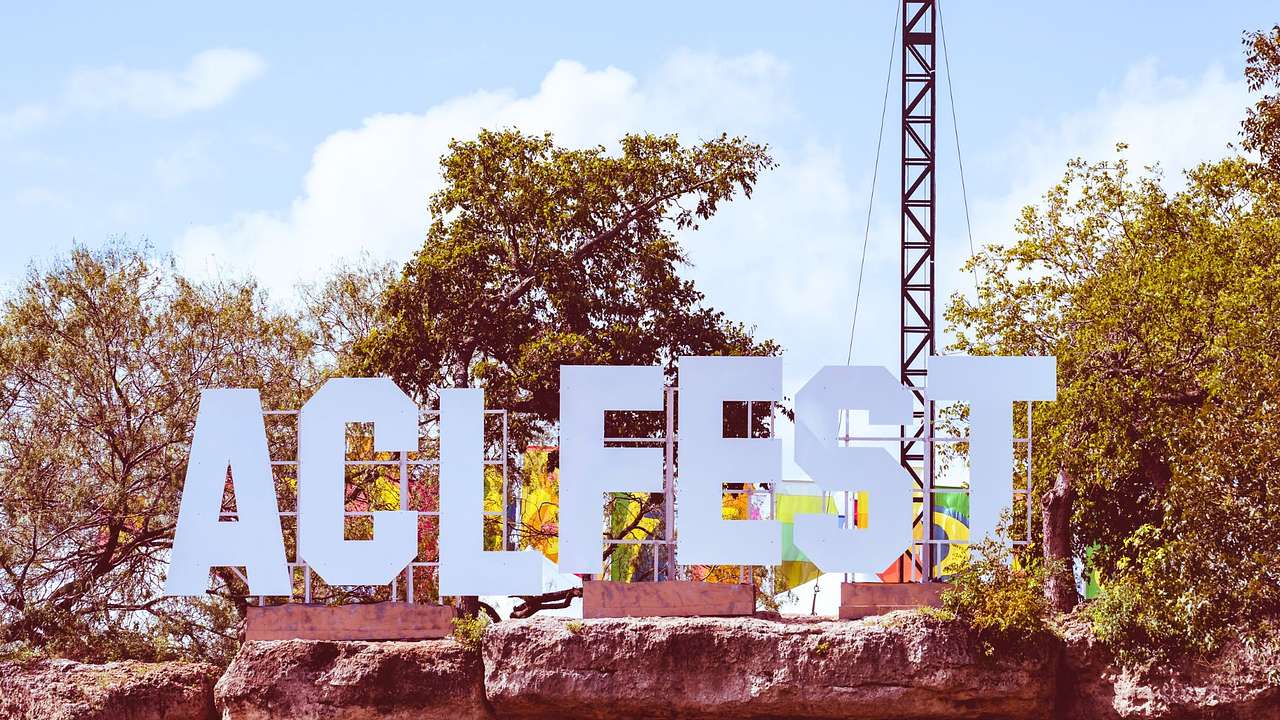 A large sign that says "ACL Fest" near trees under a blue sky with white clouds