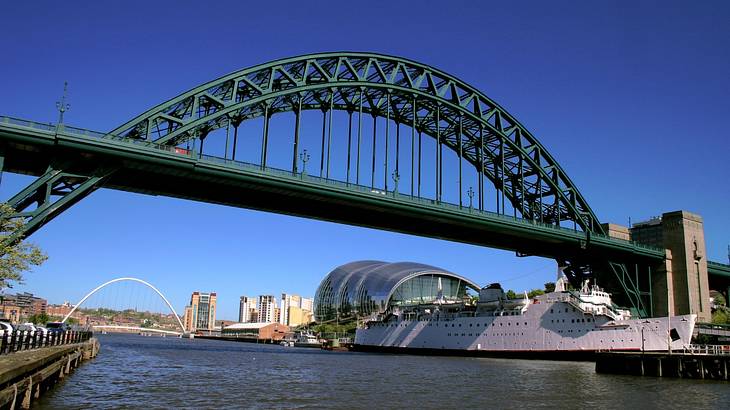A huge, steel structured bridge atop a river flowing through a city