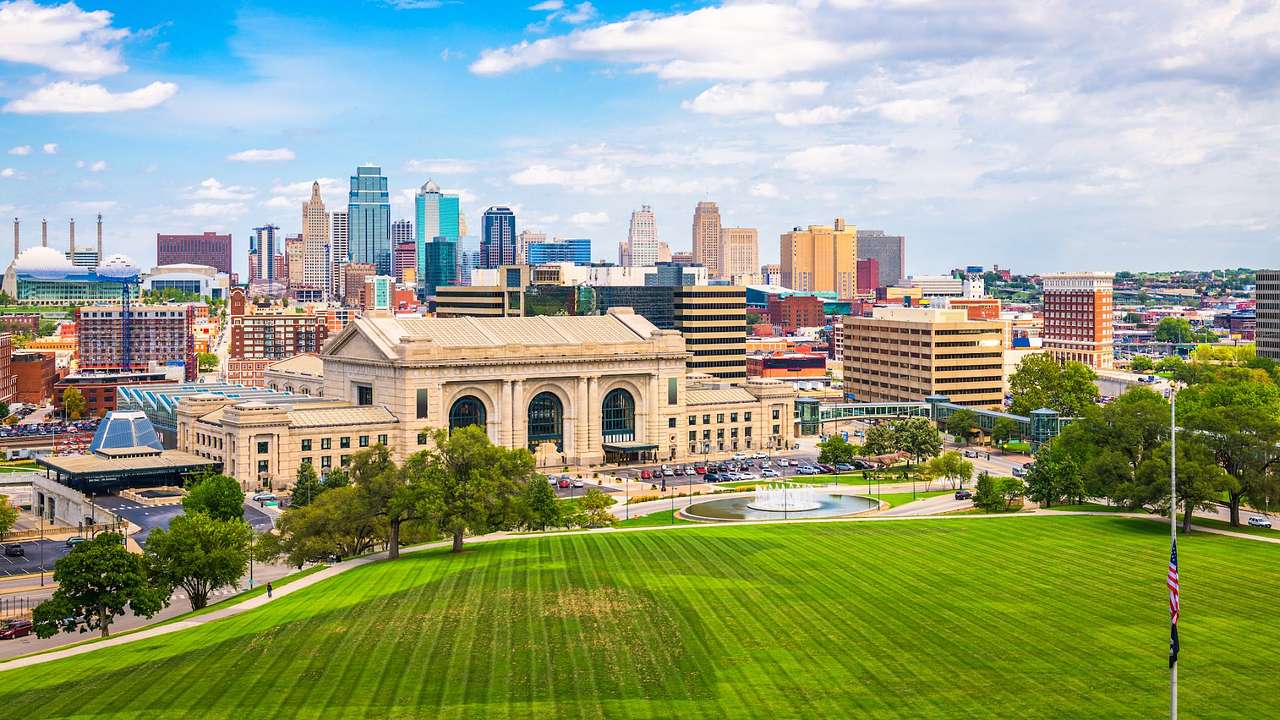 A grassy area next to a city skyline and a large stone building