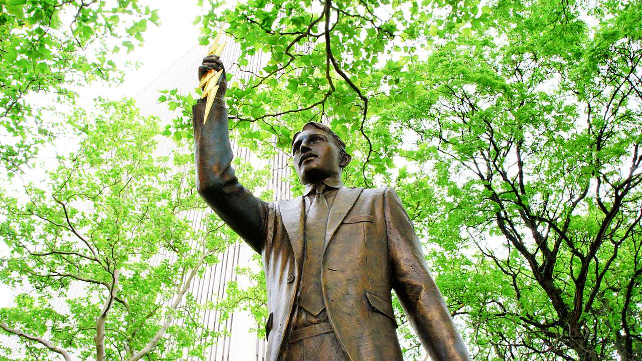 A high-angle shot of a statue of a man holding a lightning rod near trees