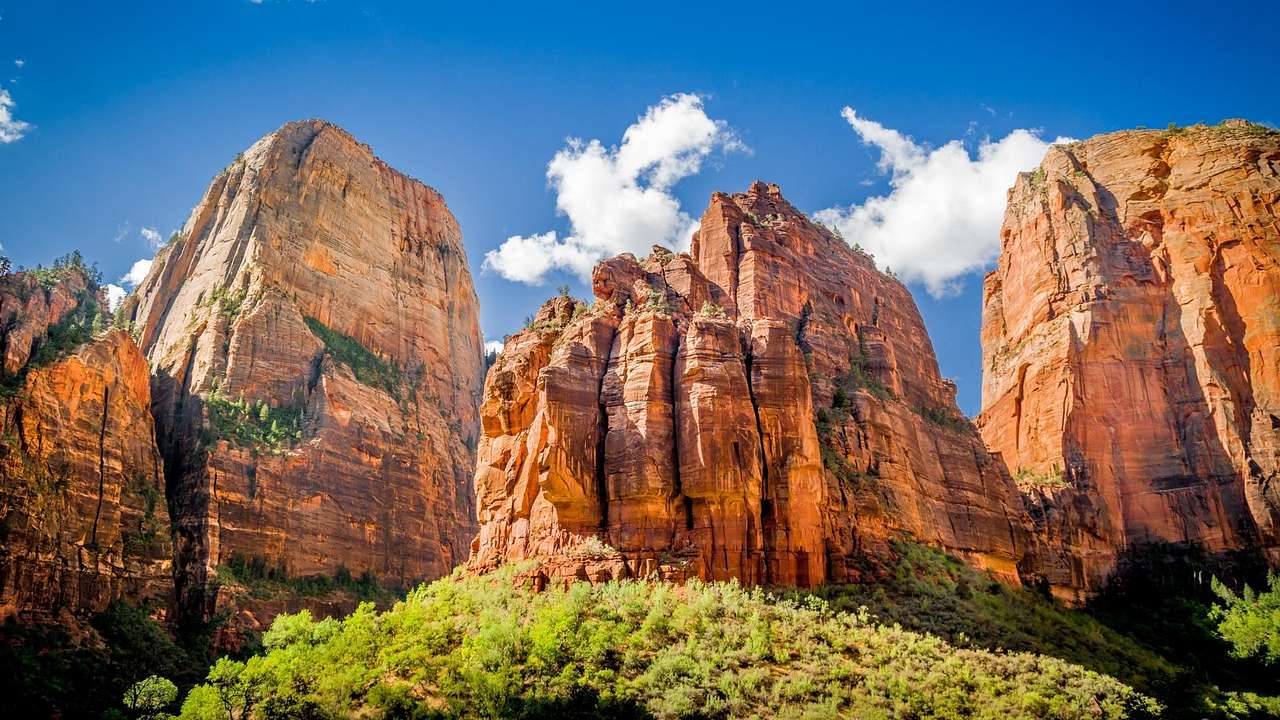 Red rock mountains with greenery in front of them under a blue sky