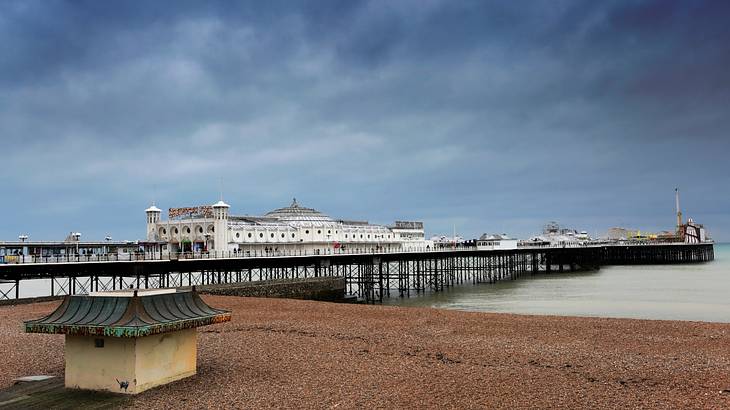 A pier over water and sand in front of a white building on a cloudy day