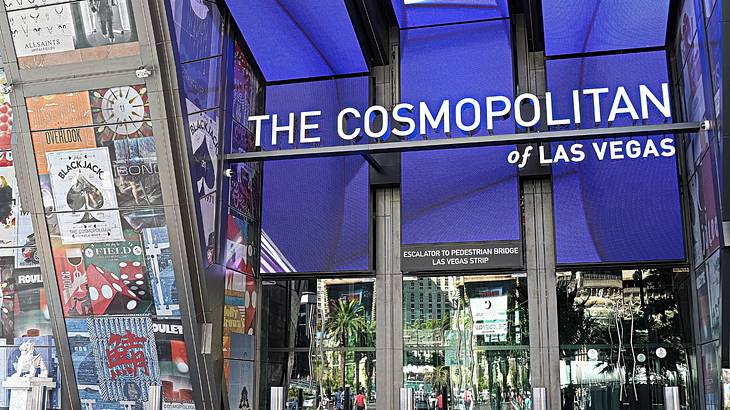 A hotel entrance with a "The Cosmopolitan of Las Vegas" sign and posters on a window