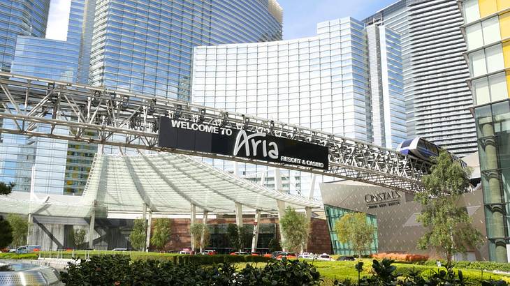 A black signboard on a hotel saying "Aria" next to greenery and buildings