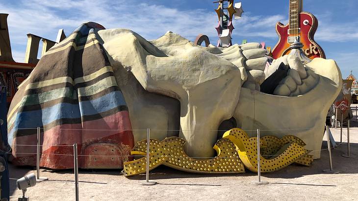 A large skull sculpture laying on sand with a guitar statue behind it