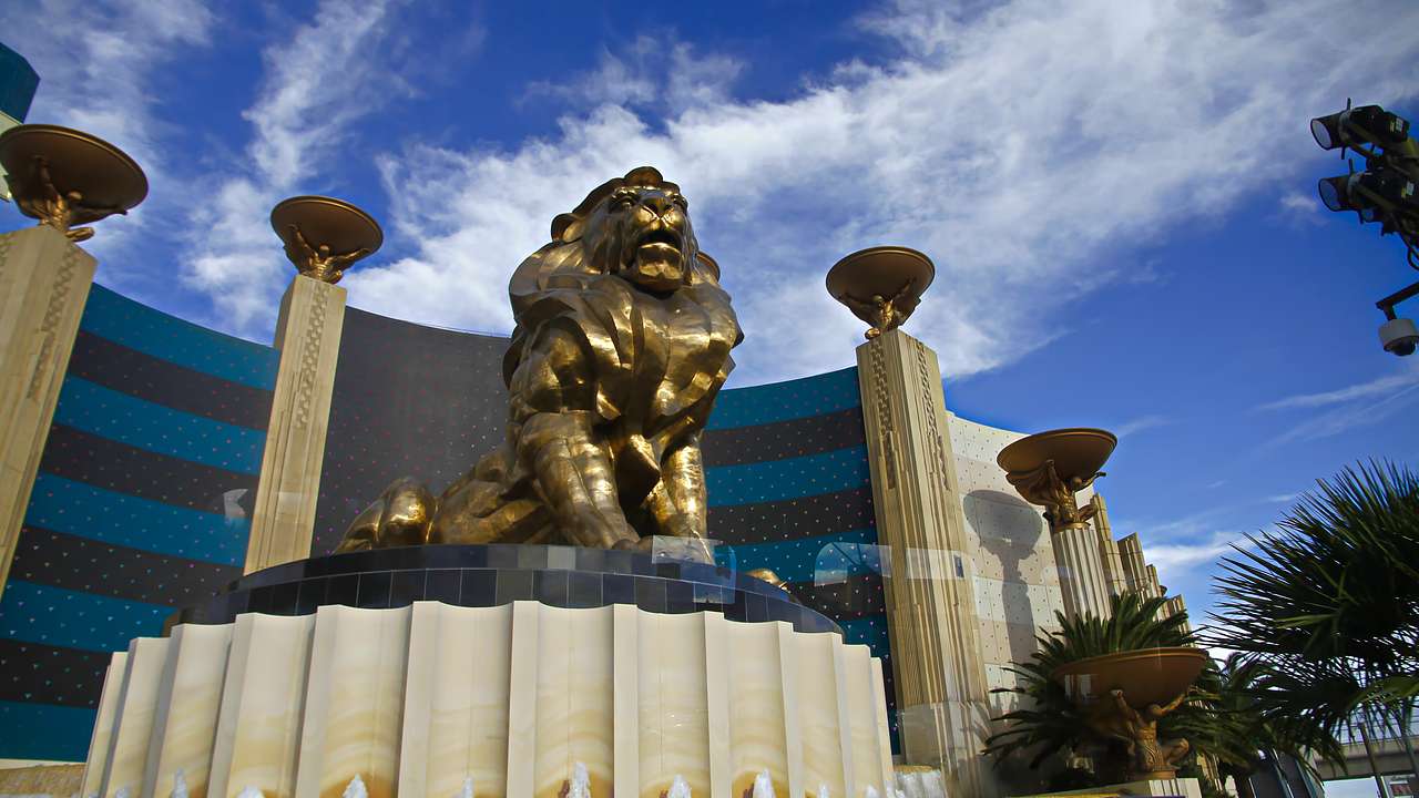 A bronze lion statue sitting on a pedestal with a tall building behind it