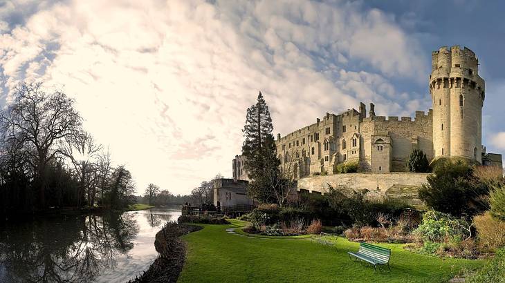A river passing along a stone castle with a gorgeous garden in front