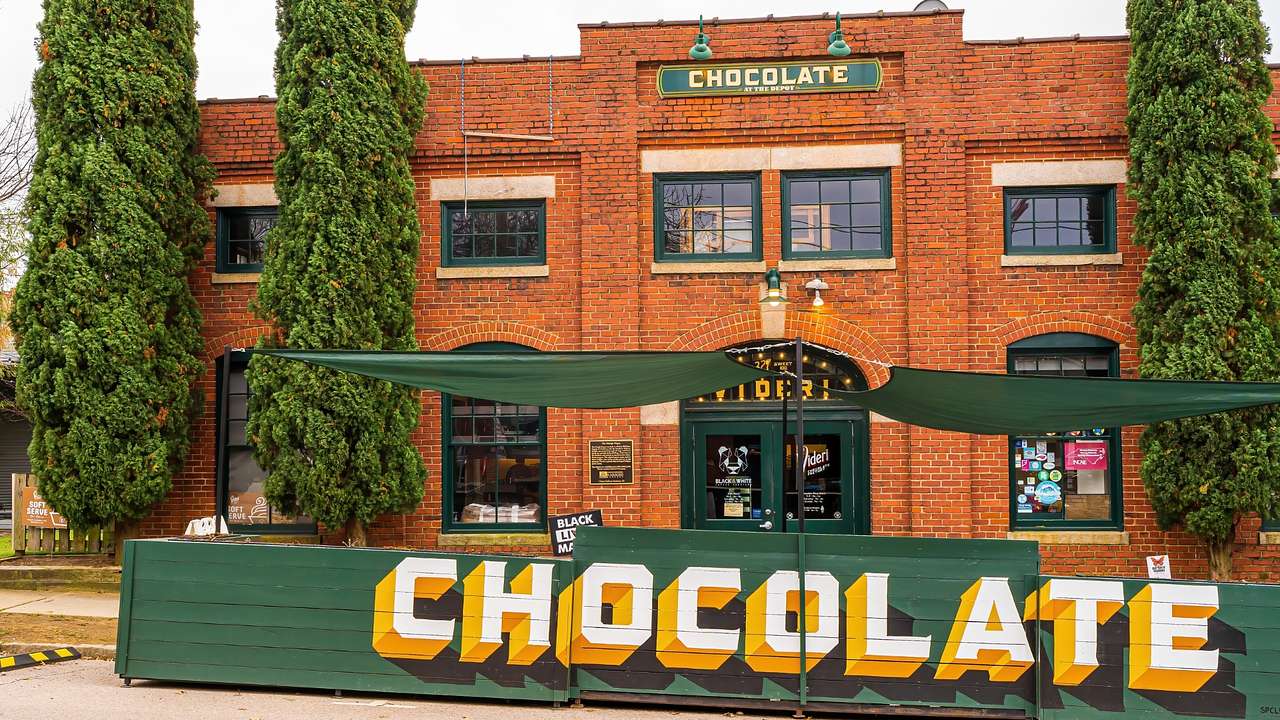 A brick building with green details next to a green sign that says "Chocolate"