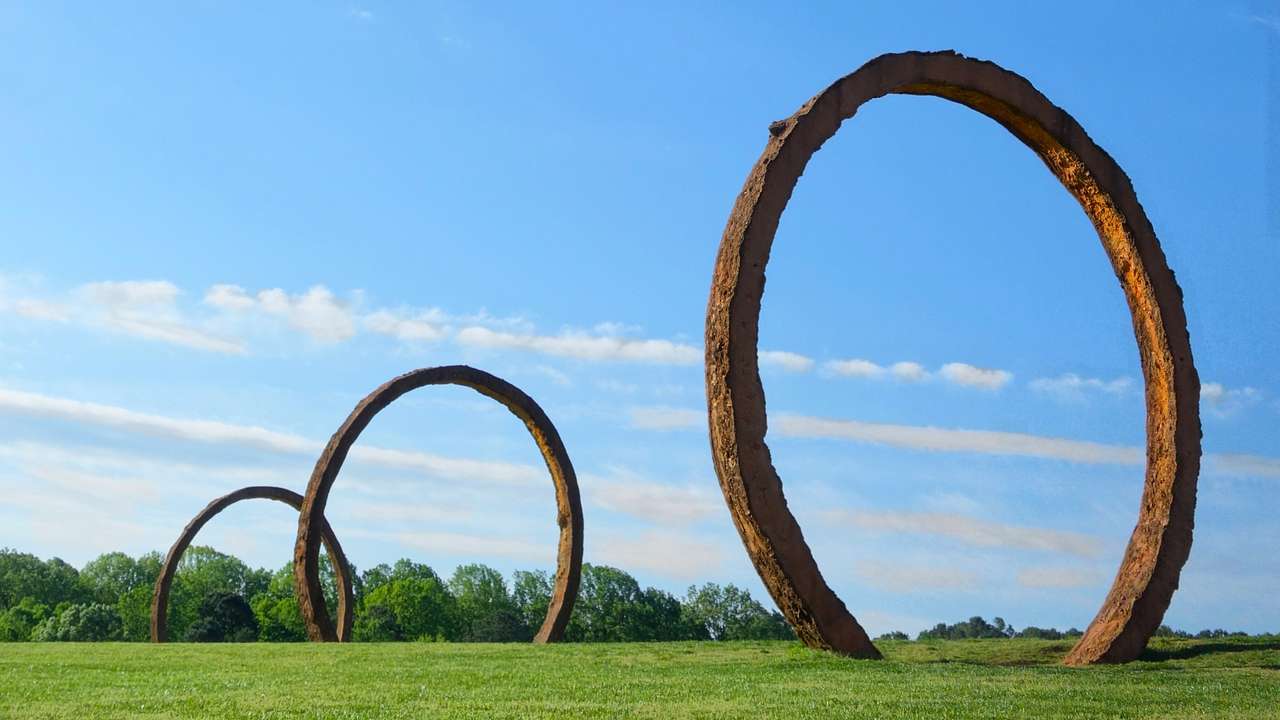 A set of three arch sculptures on the grass under a blue sky with some cloud
