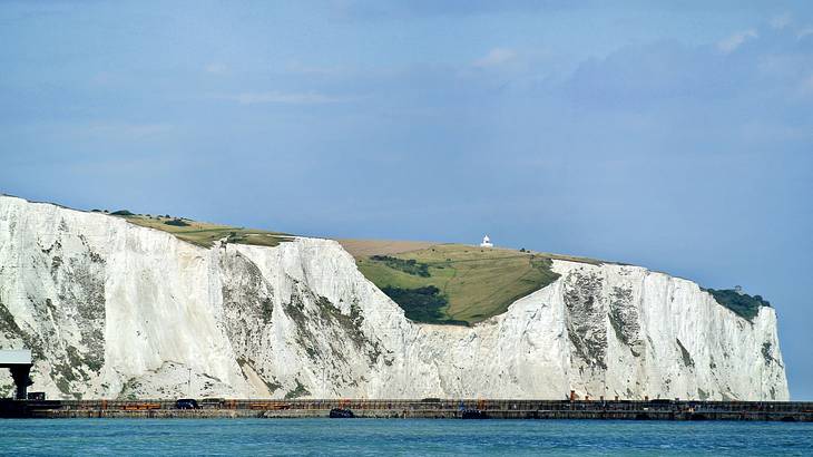 A white cliff surrounded by water with a lighthouse in the back on a sunny day