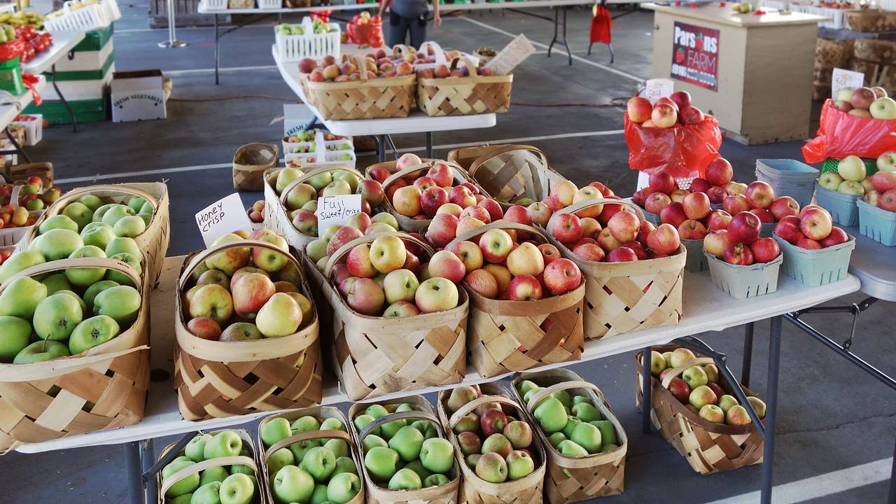 A table at a market with various types of apples in baskets