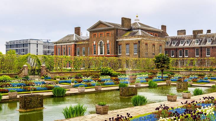 A grand brick palace with a garden full of flowers and a pond in front A grand brick palace with a garden full of flowers and a pond in front