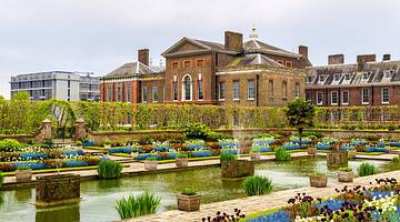 A grand brick palace with a garden full of flowers and a pond in front