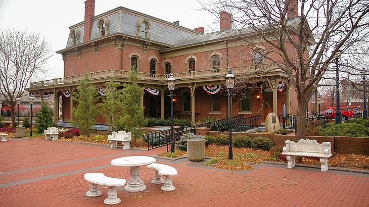 A red brick mansion with marble outdoor benches and lamp posts in front