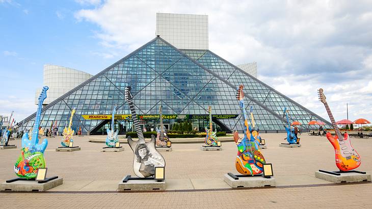 A double pyramid glass building with rows of colorful electric guitars in front