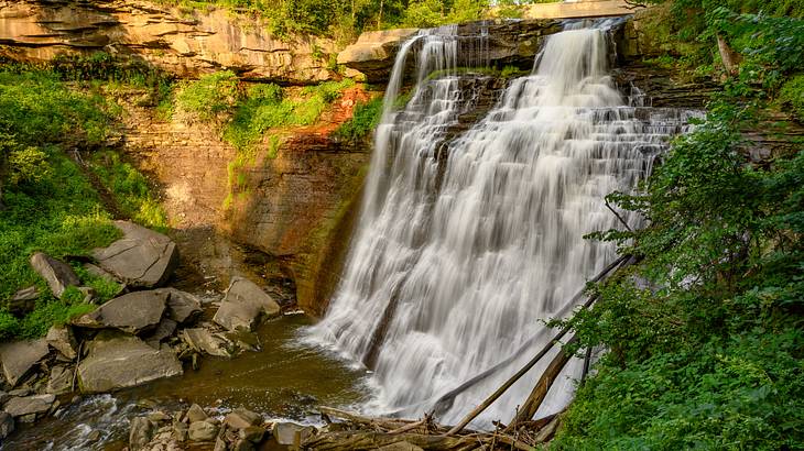 A big waterfall with a gorge beneath, surrounded by rocks and the sun shining through