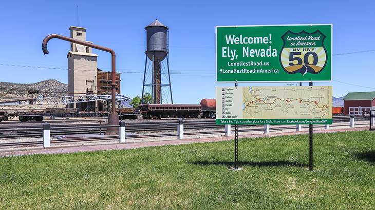 A large gray water tank and a green welcome sign with a map on a green lawn