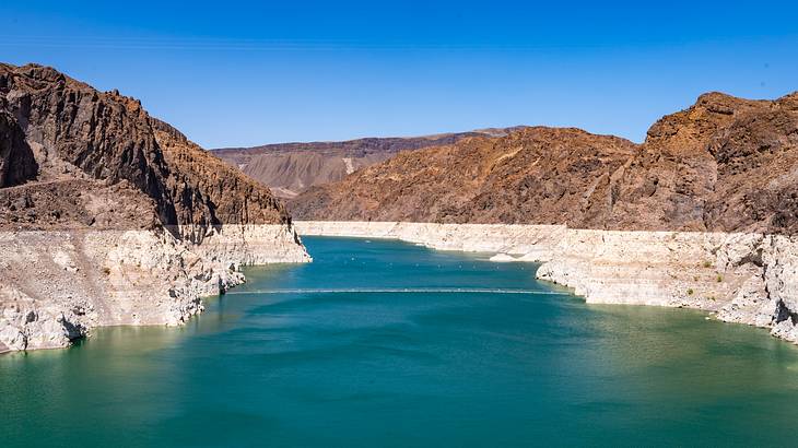 Clear blue sky and a lake with green water surrounded by dry mountains