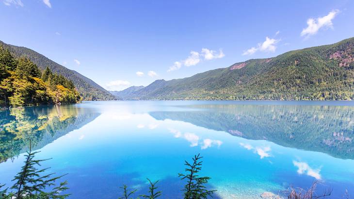 A lake with a reflection of green mountains surrounding it on a nice day