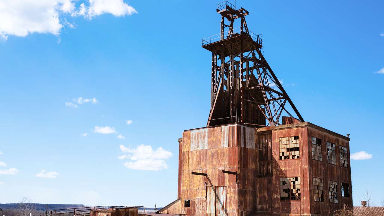 An abandoned rusty mine building next to a blue sky with some white clouds