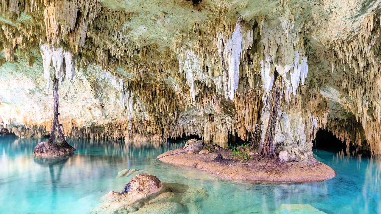A cave with clear blue water and stalagmites all around