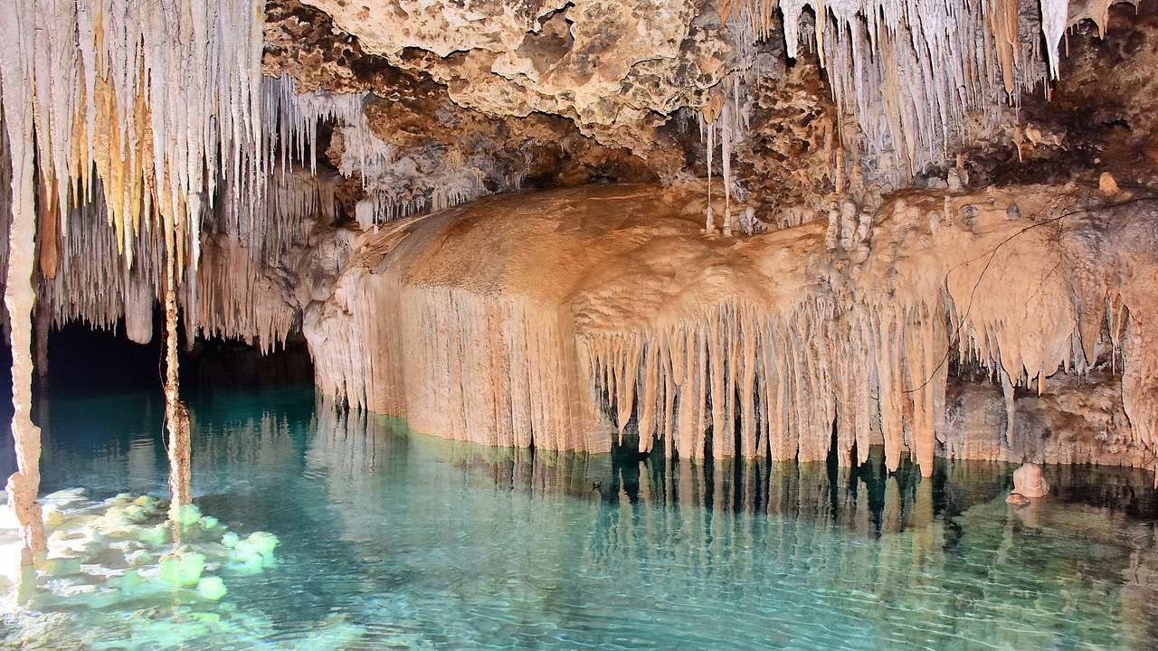 A cavern with icicle-like mineral formations with clear blue water underneath