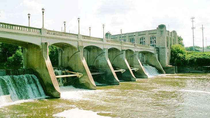 A multi-arched dam with water going through it, near a gray rectangular building