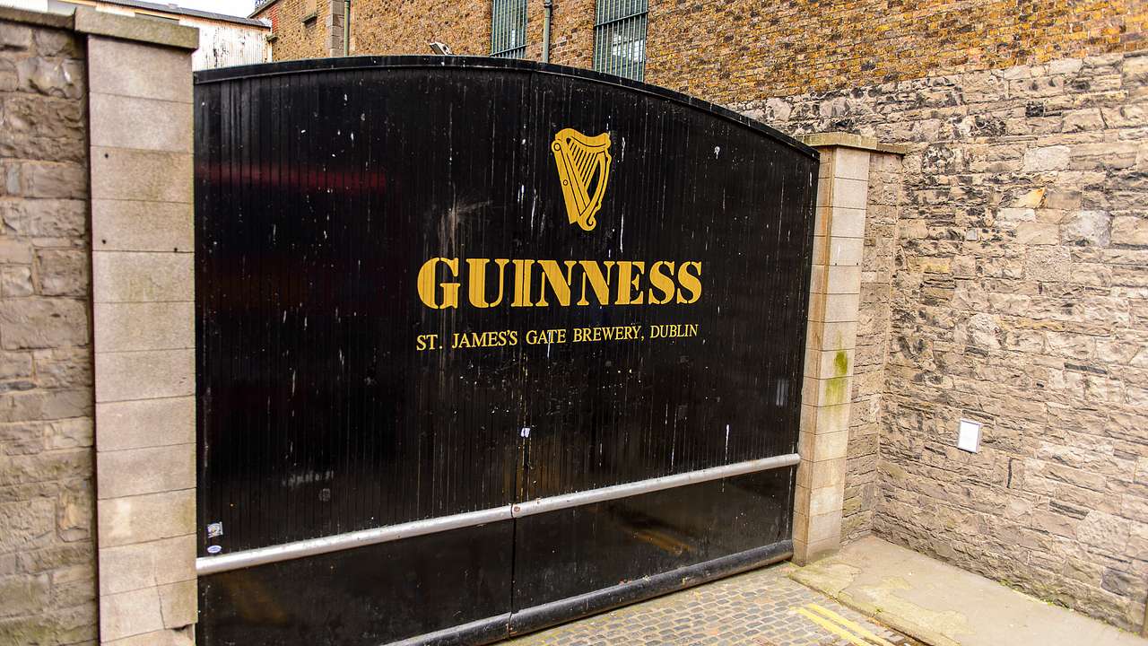 A black gate with printed text saying "Guinness" near brick walls