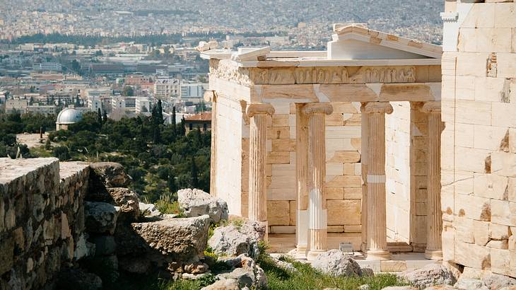 An intricate temple on a hill overlooking the city buildings in Athens