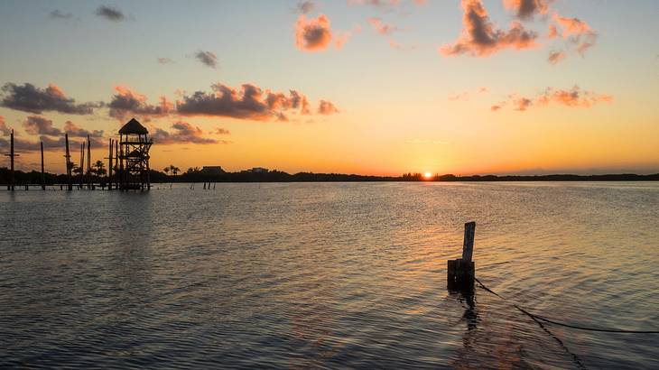 A body of water with a small structure in the distance at sunset