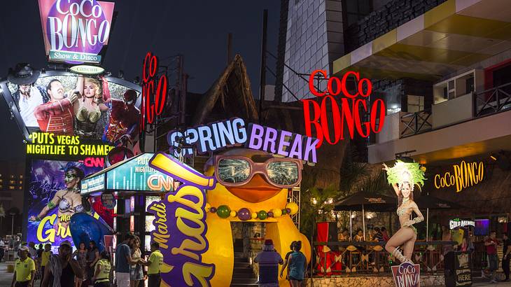 The entrance to a club at night with many neon signs and billboards on the front