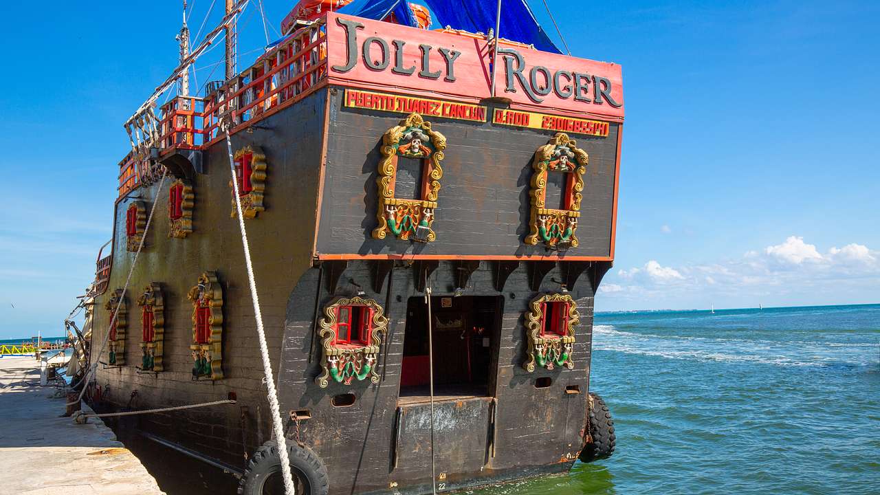 A wooden pirate ship with intricately decorated windows docked beside a pier