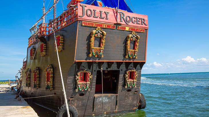 A wooden pirate ship with intricately decorated windows docked beside a pier