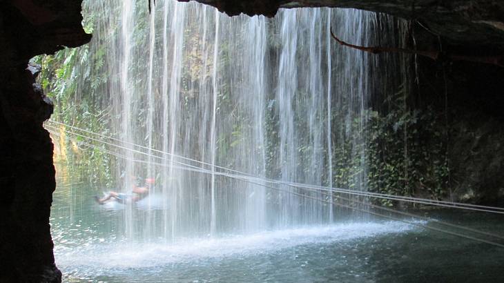 A person ziplining beside a natural waterfall into a cave