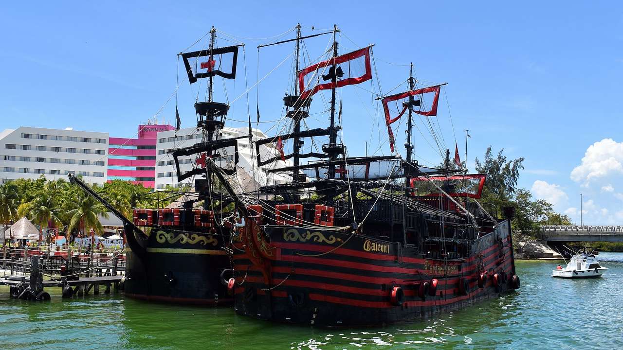 Two red and black pirate ships on the water under a blue sky