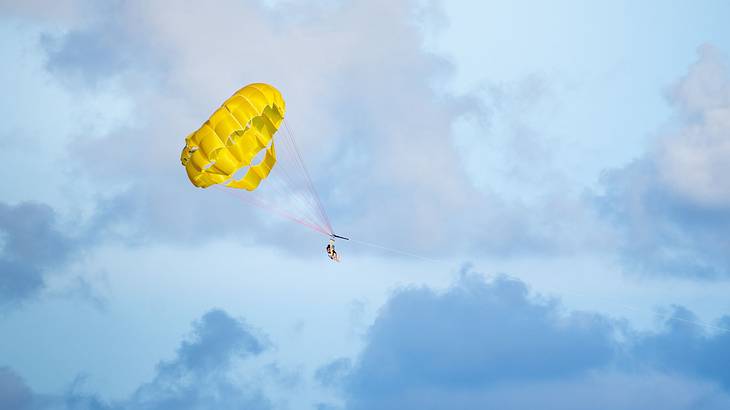 A person parasailing with a yellow parachute against the blue sky and clouds