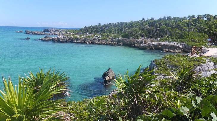 Crystal blue water surrounded by sand, rocks, and greenery under a blue sky