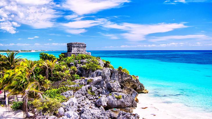 Sparkling blue ocean and sandy shores that have rocks and a stone structure on them