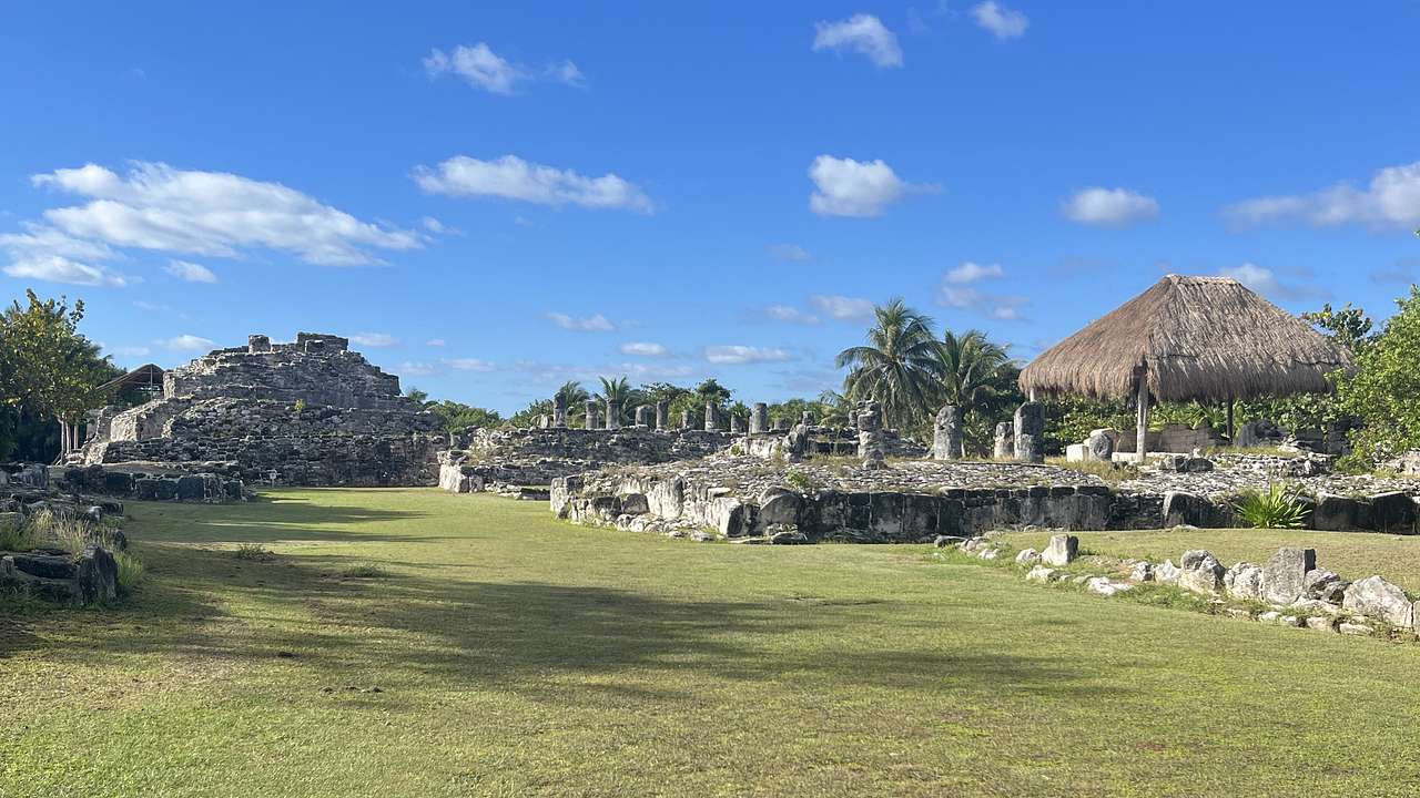 A grassy area next to ruins under a blue sky with some white clouds