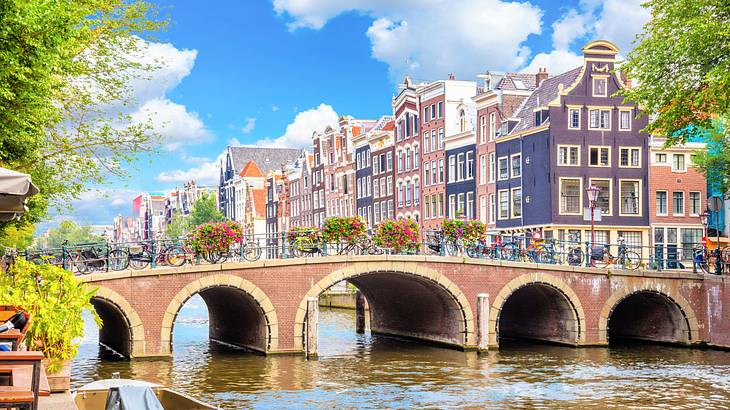 Bicycles on a bridge with arches over a canal near colorful buildings and trees