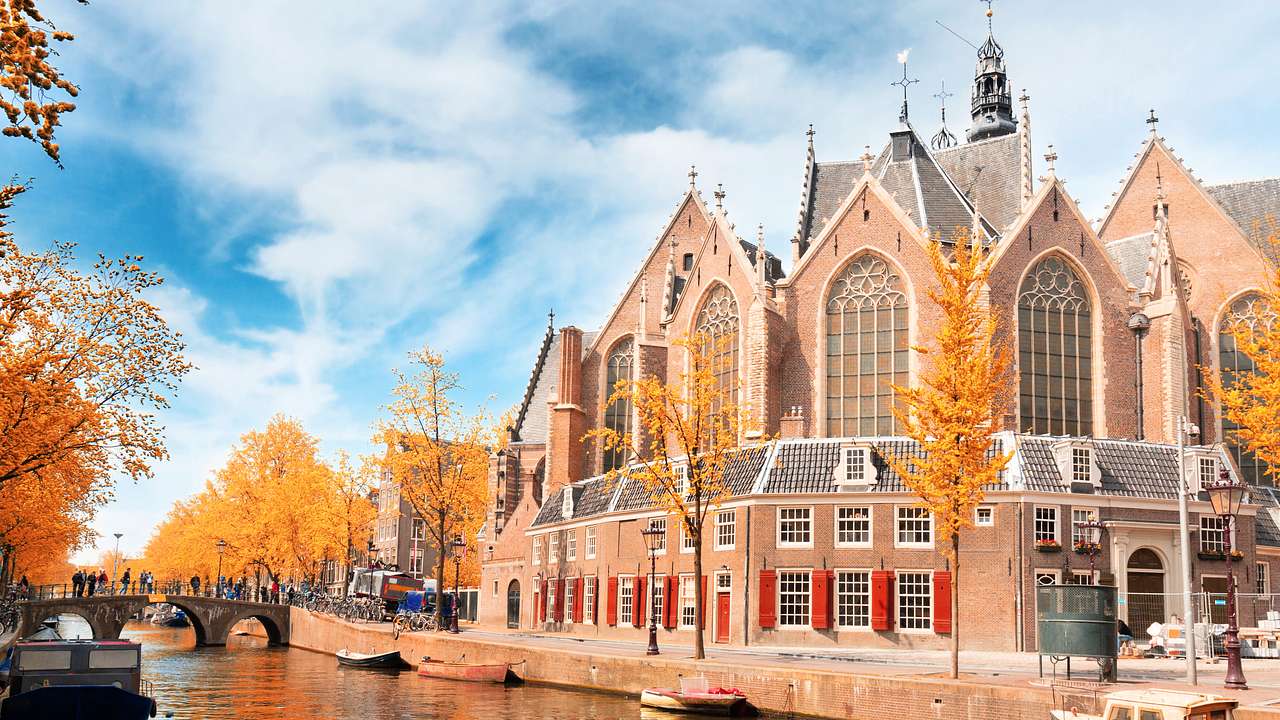 A church with many large glass windows and spires near a canal