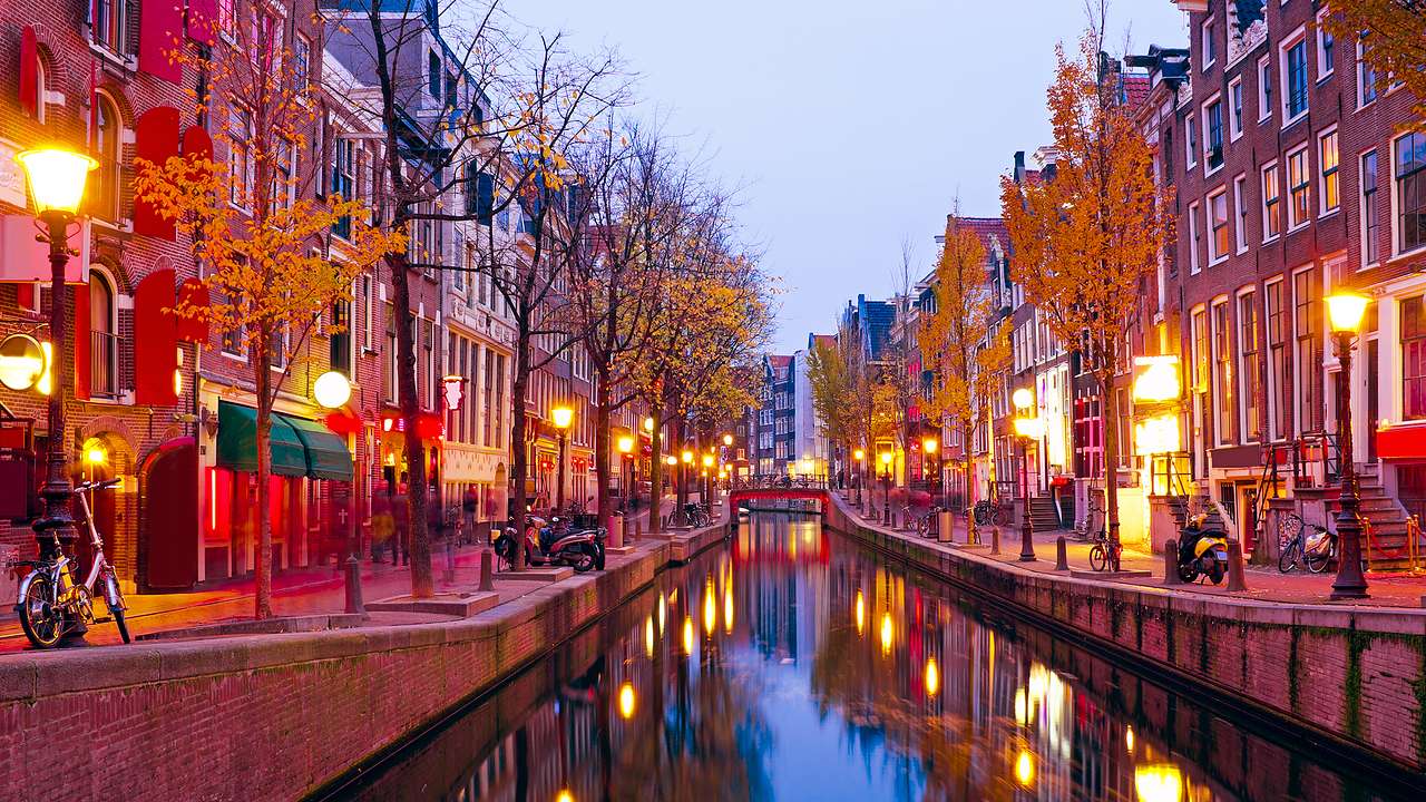 A canal with pathways on either side with lit lampposts and buildings along them